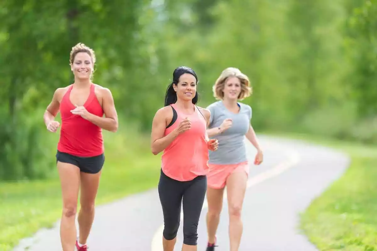 Three women dressed in sportswear running along a trail surrounded by nature