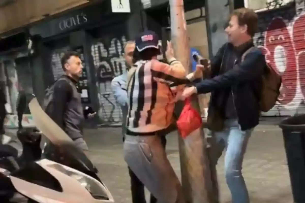 Un grupo de personas interactúa en una calle con grafitis y una motocicleta estacionada cerca.