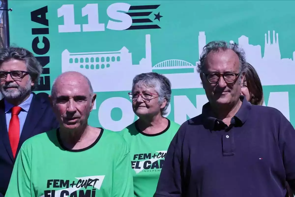 Un grupo de personas posando frente a un cartel verde que dice "11S" y "Fem + Curt El Camí".