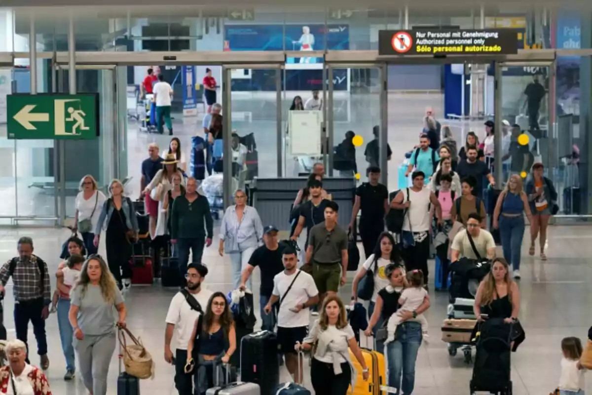 Personas caminando con maletas en un aeropuerto, con un letrero de salida de emergencia a la izquierda y un letrero de "Solo personal autorizado" arriba.