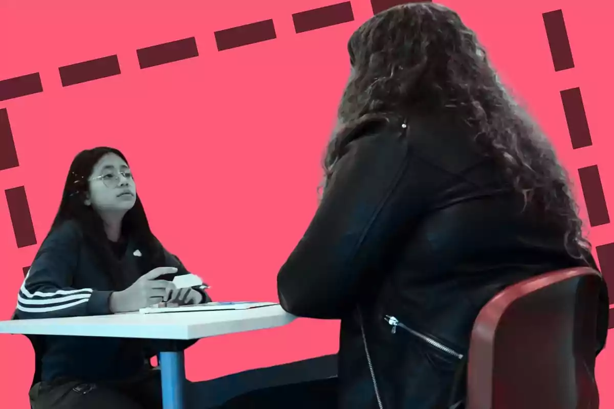 Dos personas sentadas en una mesa, una de ellas con una chaqueta de cuero y la otra con una sudadera, sobre un fondo rosa con líneas discontinuas.