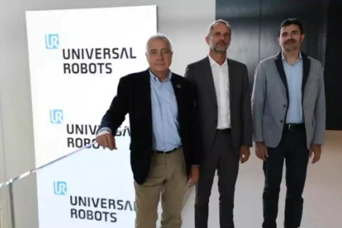 Tres hombres de pie frente a un cartel de Universal Robots.