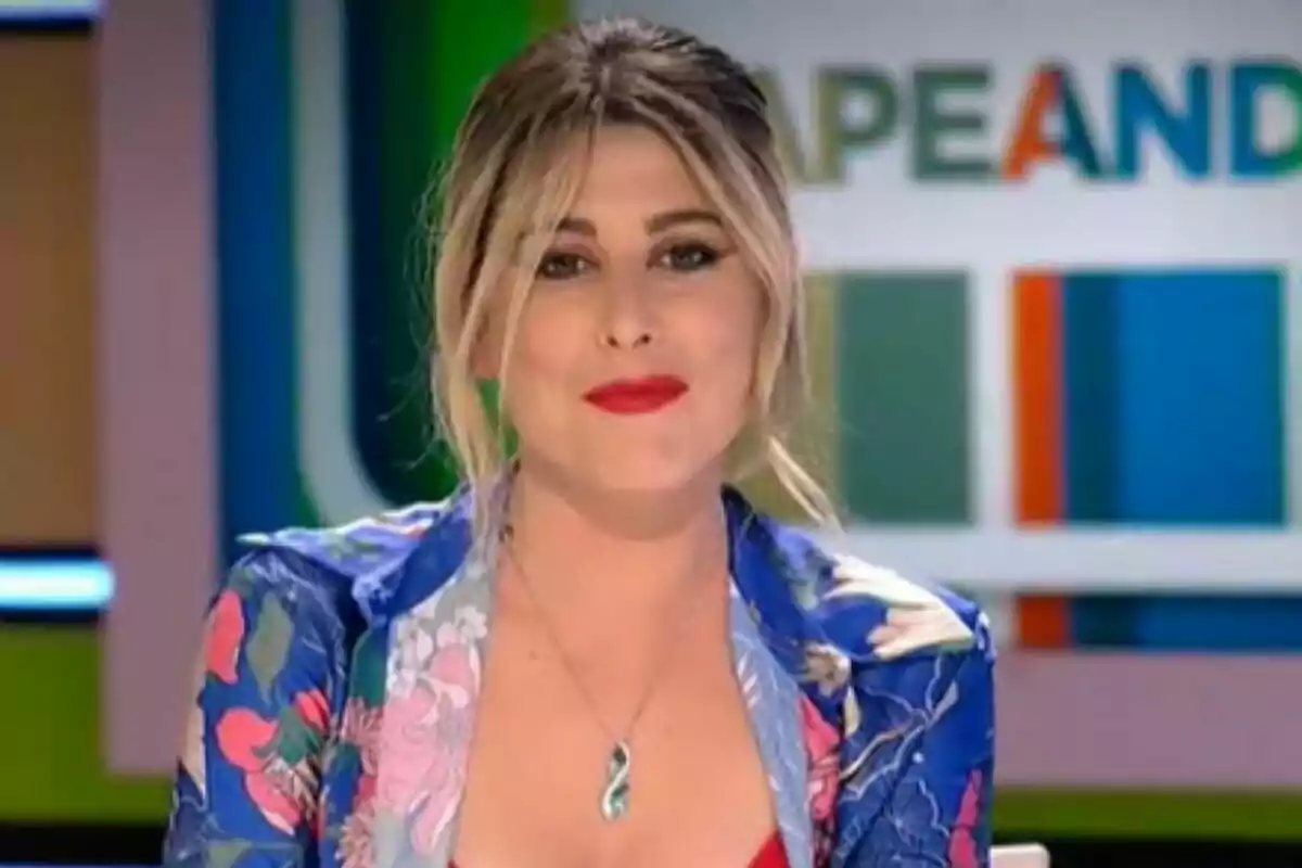 Valeria Ros con cabello rubio y labios rojos, usando una chaqueta colorida y un collar, en un set de televisión con un fondo colorido en Zapeando.