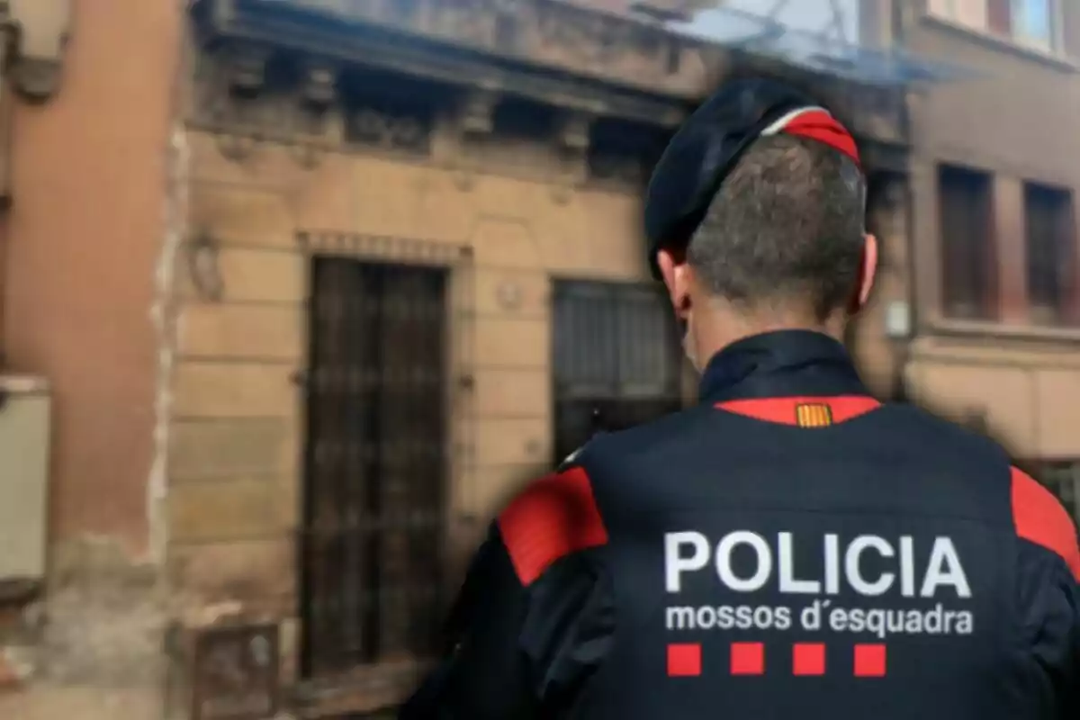 Un agente de policía de espaldas con uniforme de los Mossos d'Esquadra frente a un edificio antiguo.
