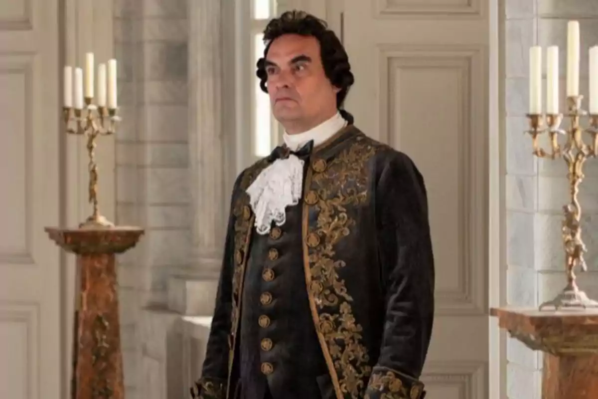 Don Hernando con peluca y traje de época elegante en una habitación decorada con candelabros y paredes clásicas. Captura de 'Valle Salvaje' Don Hernando con peluca y traje de época elegante en una habitación decorada con candelabros y paredes clásicas. Captura de 'Valle Salvaje'