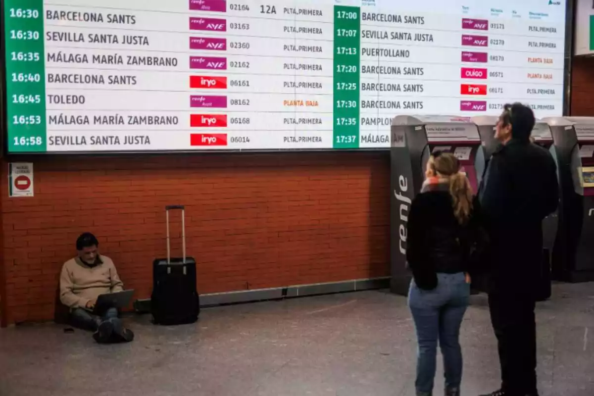 Varios viajeros delante de una pantalla anunciando las salidas y llegadas de tren