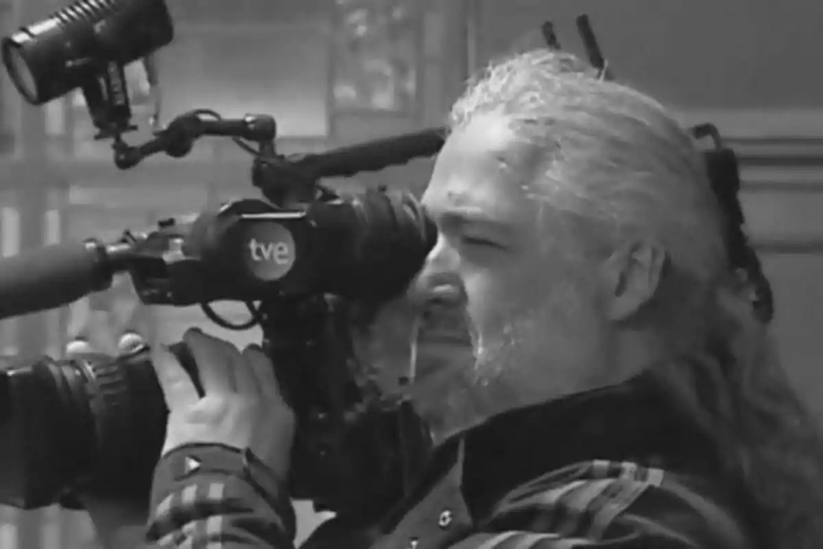 Fotografía del camarógrafo Vicente Gil Díaz con cabello largo y canoso está operando una cámara de televisión con el logotipo de "tve".