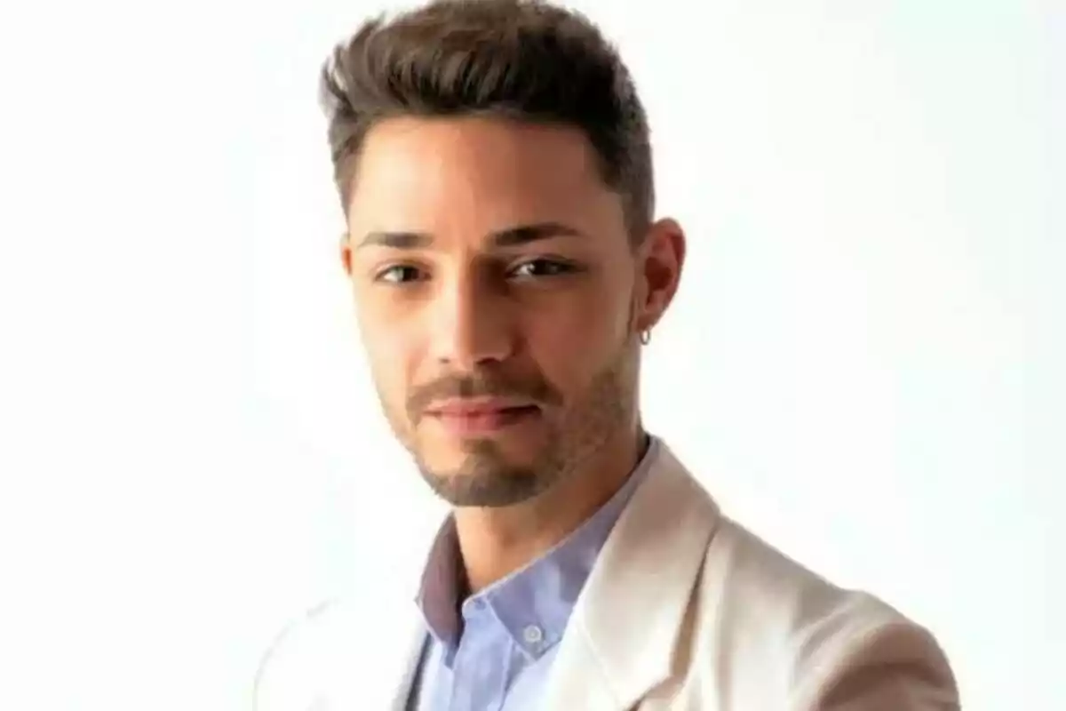 Un hombre joven con barba y cabello corto lleva una camisa azul y una chaqueta clara, mirando a la cámara con una expresión neutral. Un hombre joven con barba y cabello corto lleva una camisa azul y una chaqueta clara, mirando a la cámara con una expresión neutral.