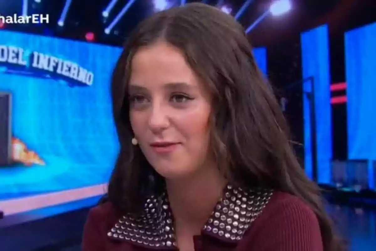 Victoria Federica con cabello largo y oscuro, usando un micrófono de diadema, está en El Hormiguero con luces y pantallas azules de fondo.