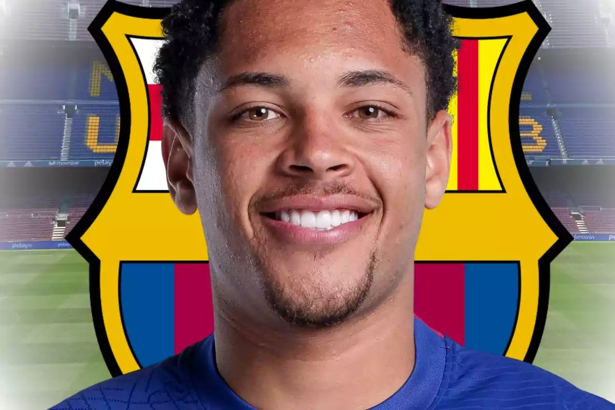 Un hombre sonriente con una camiseta azul frente al escudo del FC Barcelona.