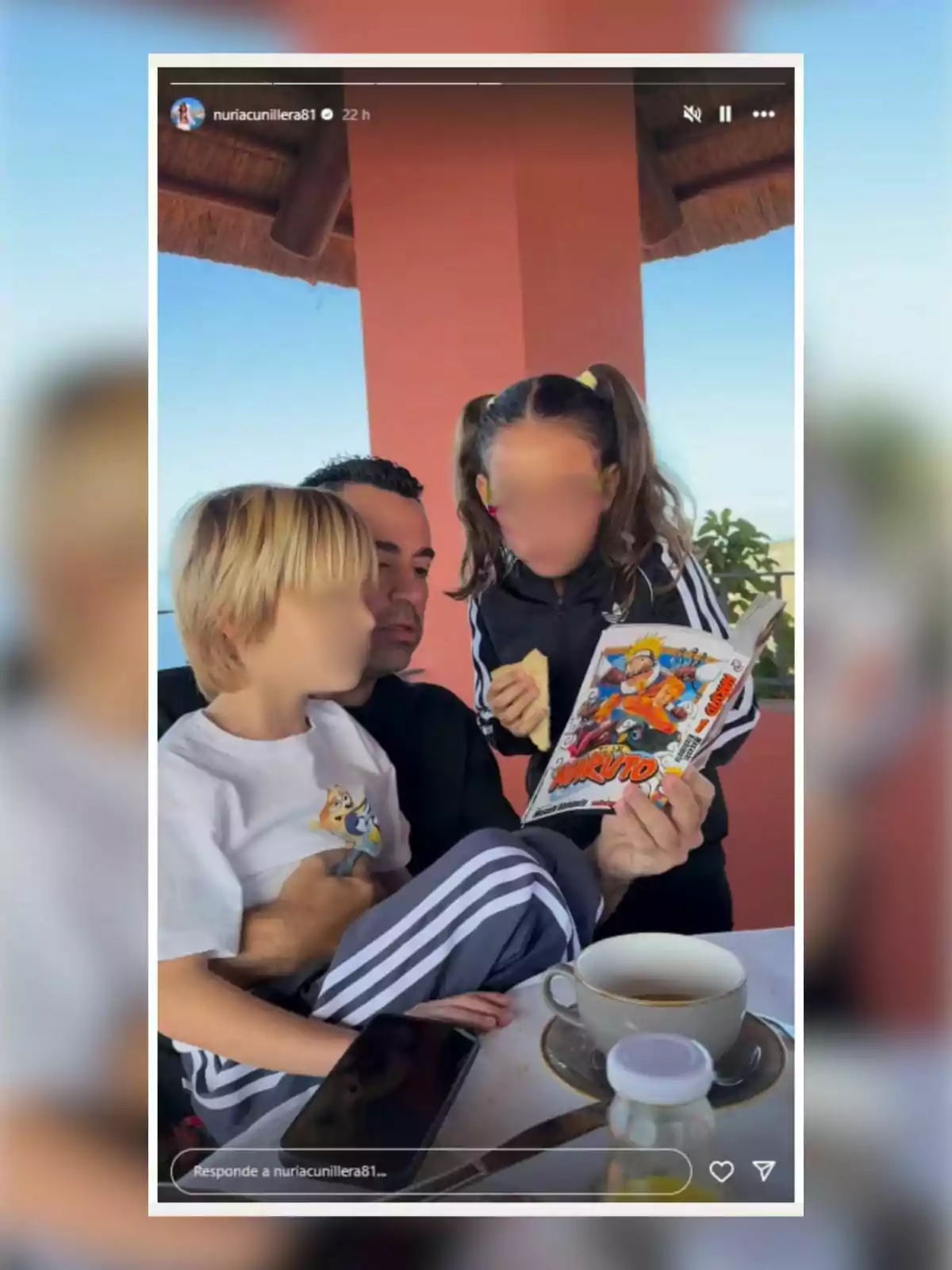 Una persona sentada con dos niños, uno de ellos sostiene un libro de Naruto mientras están en una terraza con una taza de café sobre la mesa. Una persona sentada con dos niños, uno de ellos sostiene un libro de Naruto mientras están en una terraza con una taza de café sobre la mesa.