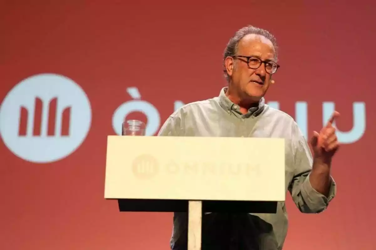 Hombre hablando en un podio con un fondo rojo y el logo de Òmnium.