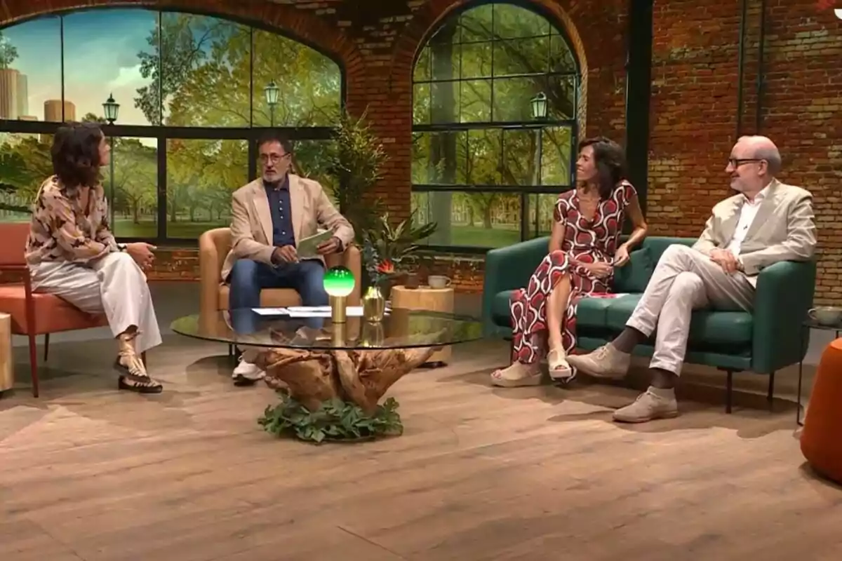 Xavier Grasset junto a Antoni Bassas, Alba Alfageme y Maria Juan sentadas en un set de televisión con una mesa de centro de cristal y un fondo que simula un parque en La Selva.