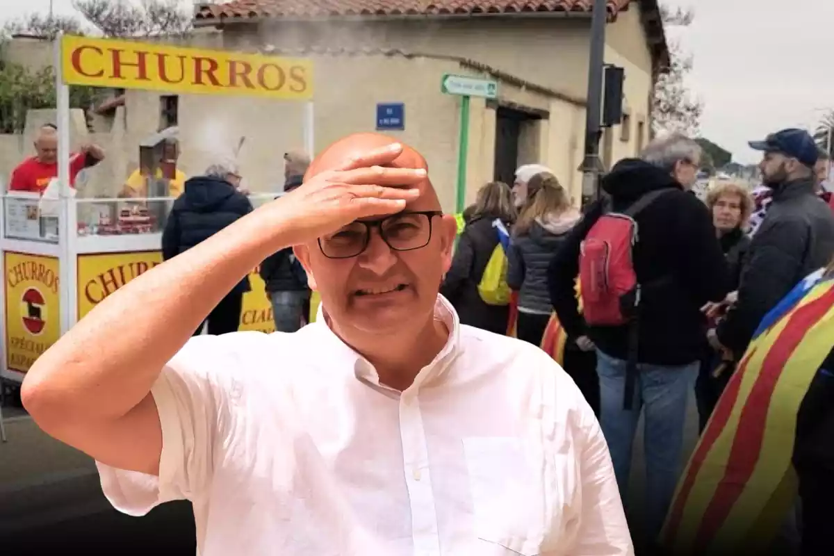 plano medio de Xavier Rius poniéndose la mano sobre su frente y con cara de preocupación, detrás de él un plano general de unos manifestantes catalanes independentistas comprando churros en un puesto ambulante a su izquierda