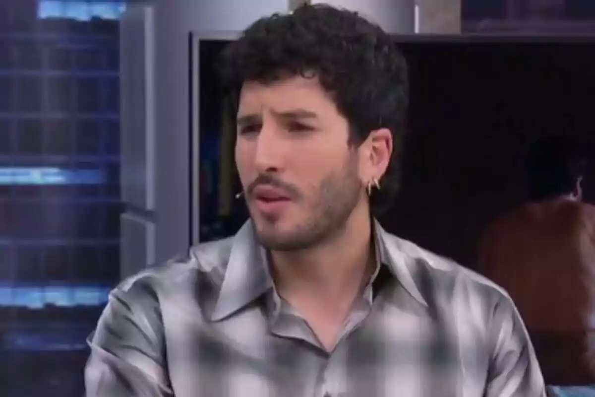 Sebastián Yatra con barba y cabello rizado lleva una camisa a cuadros y está en 'El Hormiguero'.