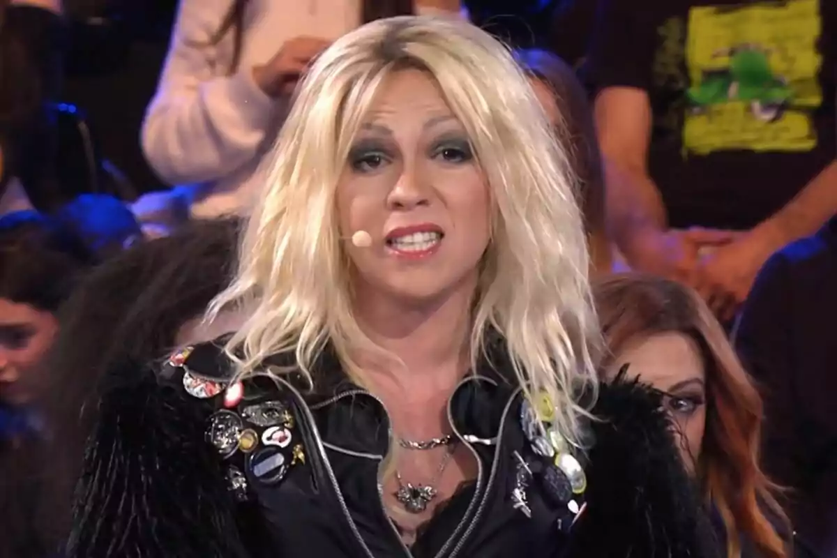 Yenesi con peluca rubia y chaqueta con parches y botones está hablando en un escenario con público de fondo en Tu Cara Me Suena.