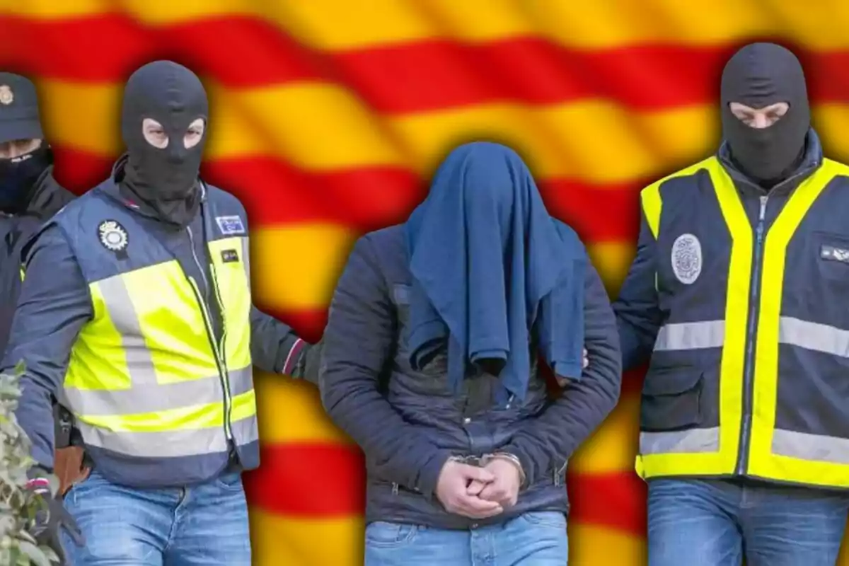 Policías enmascarados escoltan a un detenido con la cabeza cubierta frente a una bandera de Cataluña.