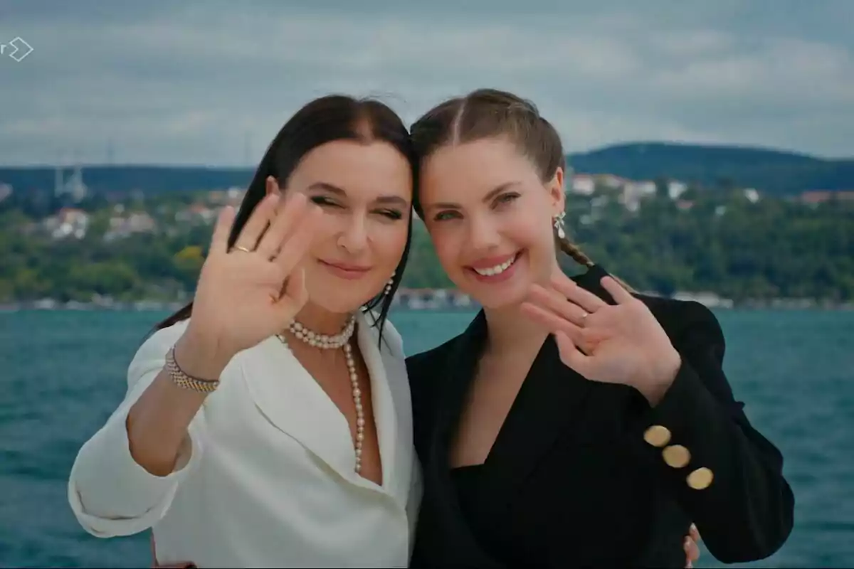 Yildiz y Ender sonrientes saludando con la mano frente a un paisaje costero en el final de Pecado Original