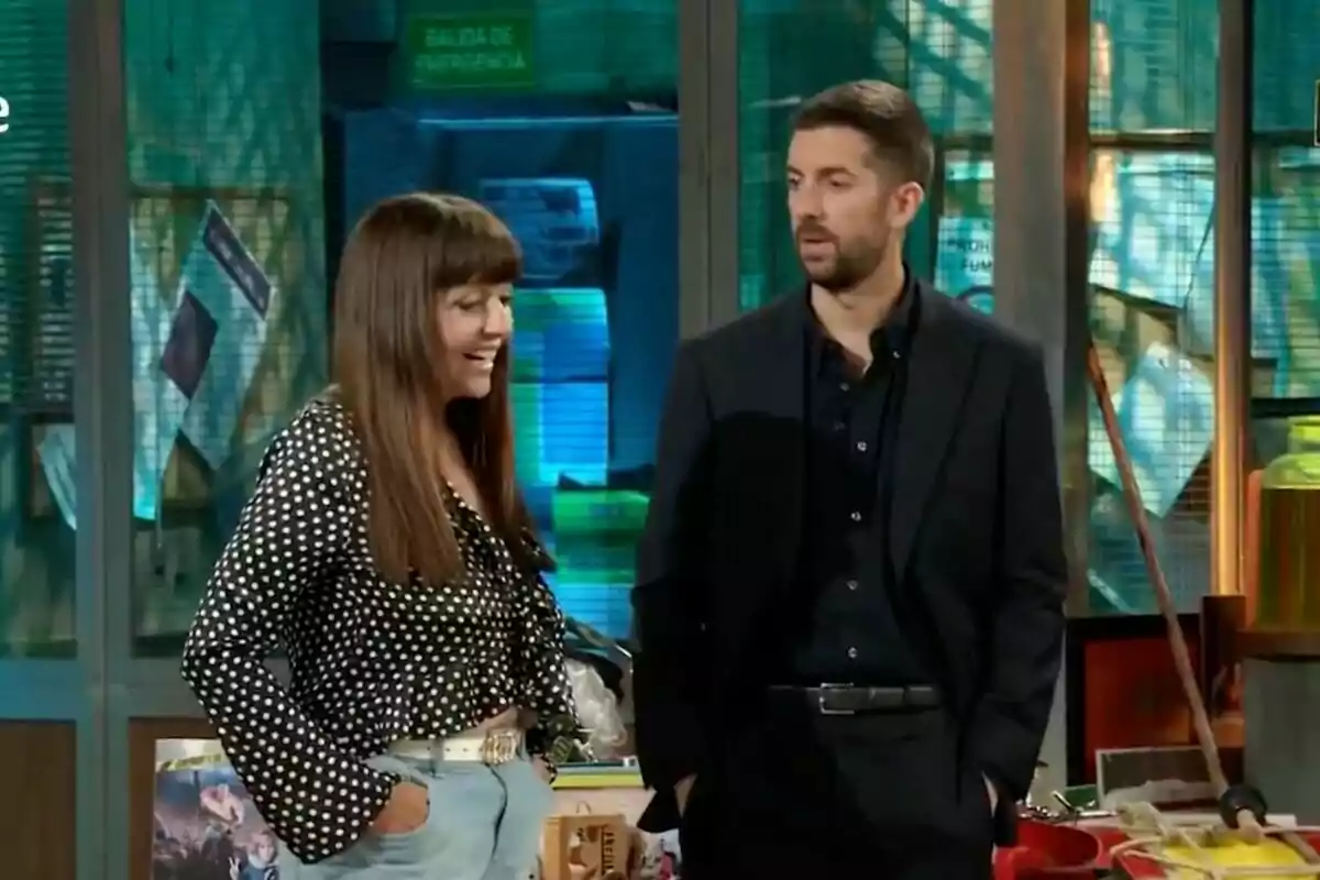 Yolanda Ramos y David Broncano conversan en 'La Revuelta' con fondo de objetos y letreros, una mujer sonríe mientras un hombre la observa. Yolanda Ramos y David Broncano conversan en 'La Revuelta' con fondo de objetos y letreros, una mujer sonríe mientras un hombre la observa.