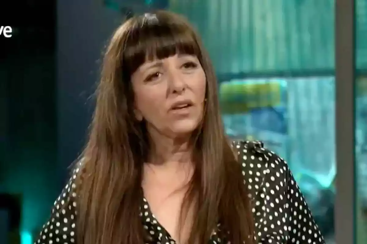 Yolanda Ramos con cabello largo y lacio con flequillo, usando una blusa negra con lunares blancos, en 'La Revuelta' con fondo desenfocado.